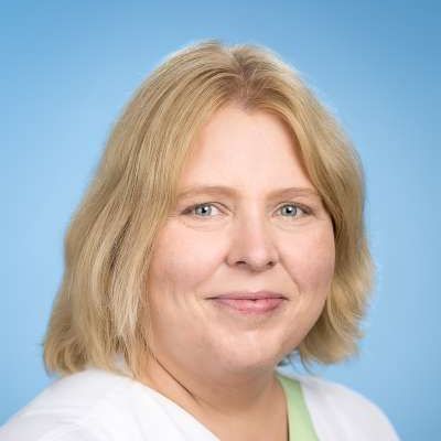Eine Frau mit blonden Haaren und grünen Augen lächelt in die Kamera.