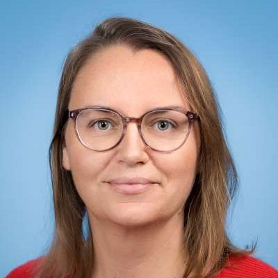 Eine Frau mit Brille und rotem Hemd lächelt in die Kamera.