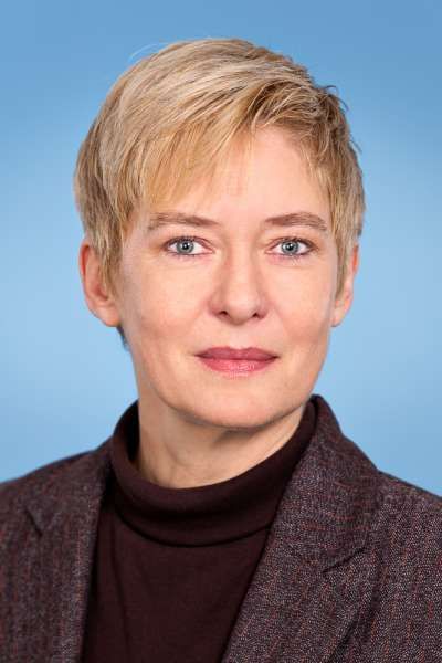 Eine Frau mit kurzen blonden Haaren trägt einen Anzug und einen Rollkragenpullover.
