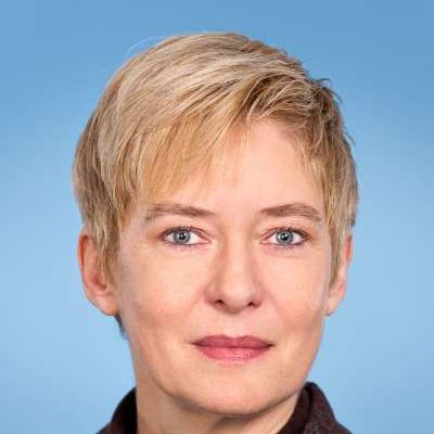 Eine Nahaufnahme des Gesichts einer Frau mit kurzen blonden Haaren und blauen Augen.