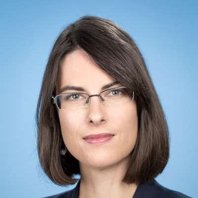 Eine Frau mit Brille und Jacke lächelt in die Kamera.
