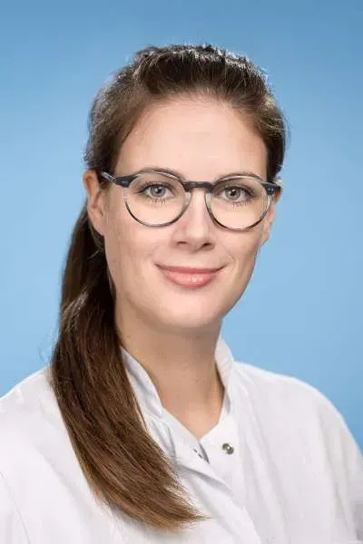 Eine Frau mit Brille und weißem Kittel lächelt in die Kamera.