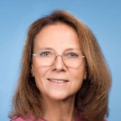Eine Frau mit Brille und rosa Hemd lächelt in die Kamera.
