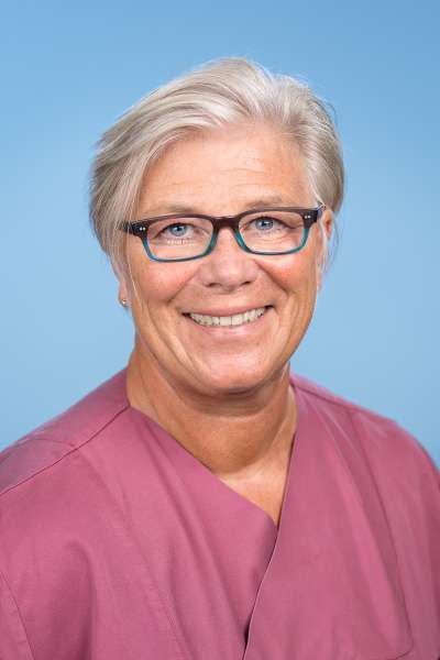 Eine Frau mit Brille und rosa OP-Kittel lächelt in die Kamera.
