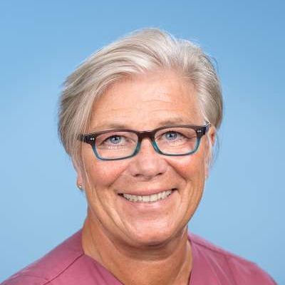 Eine Frau mit Brille und rosa Hemd lächelt in die Kamera.