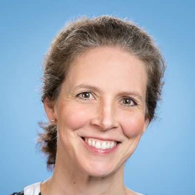 Vor einem blauen Hintergrund lächelt eine Frau in die Kamera.