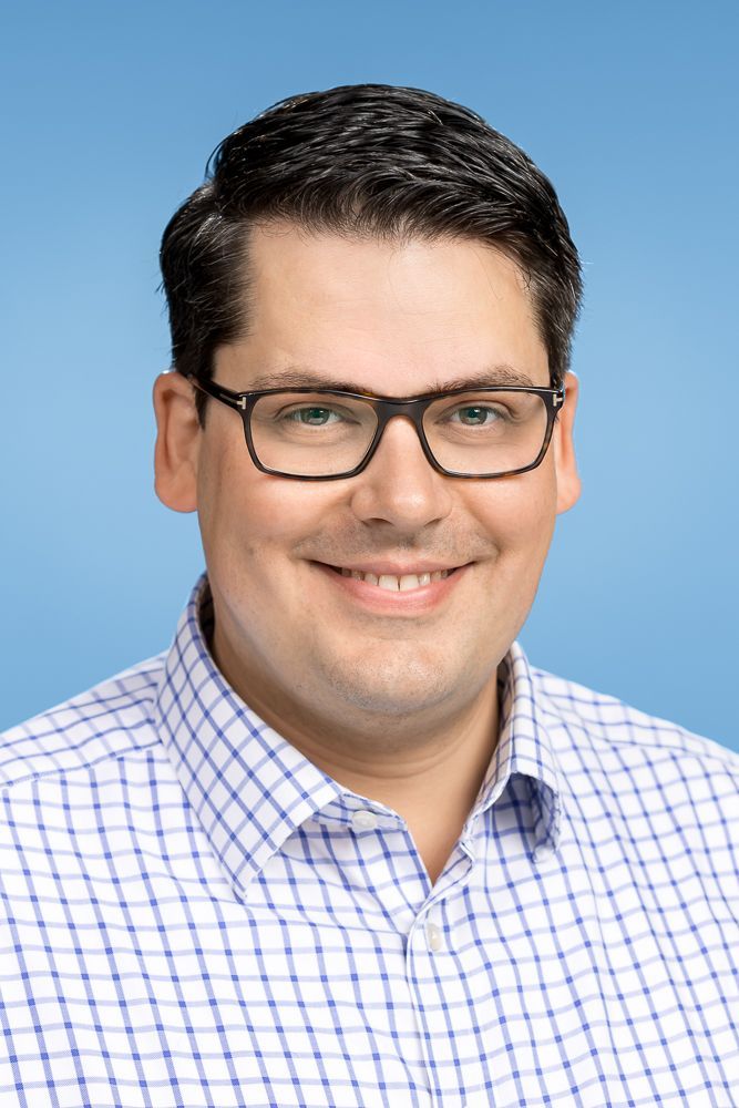 Ein Mann mit Brille und kariertem Hemd lächelt in die Kamera.