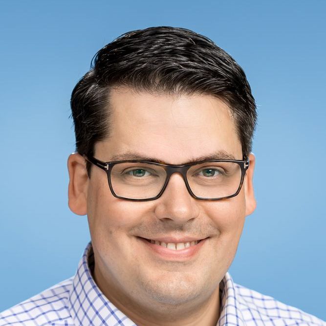 Ein Mann mit Brille und kariertem Hemd lächelt in die Kamera.