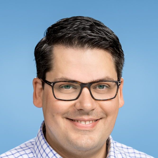 Ein Mann mit Brille und kariertem Hemd lächelt in die Kamera