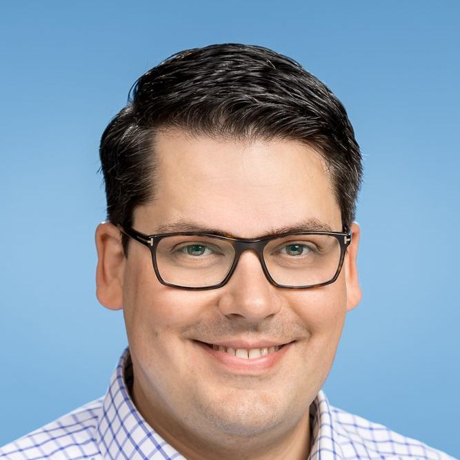 Ein Mann mit Brille und kariertem Hemd lächelt in die Kamera.