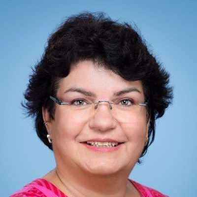 Eine Frau mit Brille und rosa Hemd lächelt in die Kamera.