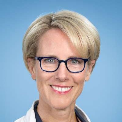 Eine Frau mit Brille und weißem Kittel lächelt in die Kamera.
