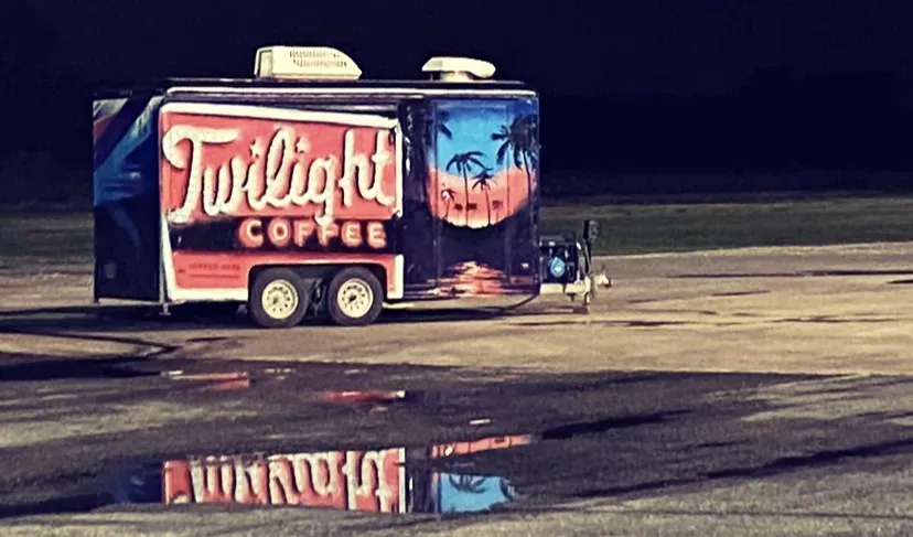 Twilight Coffee trailer parked at night, with palm-tree sunset artwork and a reflection on wet pavement