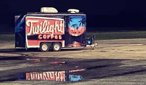 Twilight Coffee trailer parked at night, with palm-tree sunset artwork and a reflection on wet pavement