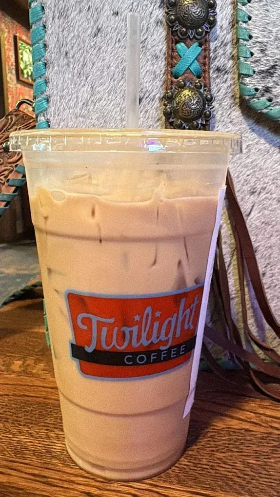 Iced coffee in a clear plastic cup with a Twilight Coffee logo, on a table.