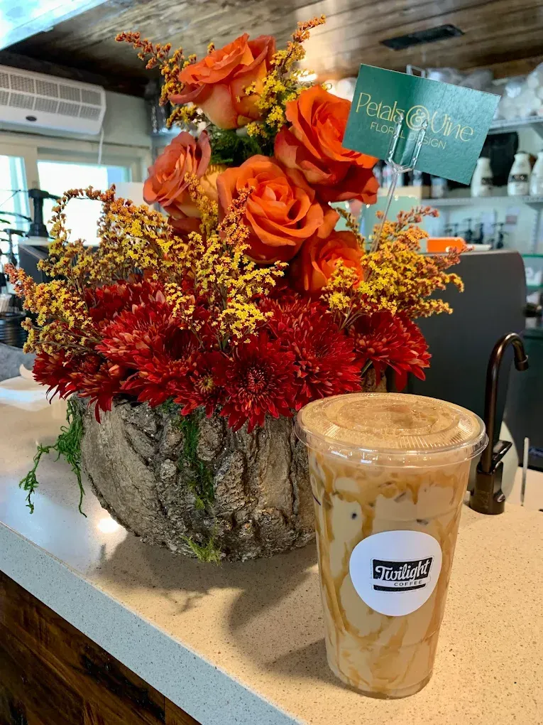 Orange and red floral arrangement in a metal vase beside a latte on a café counter