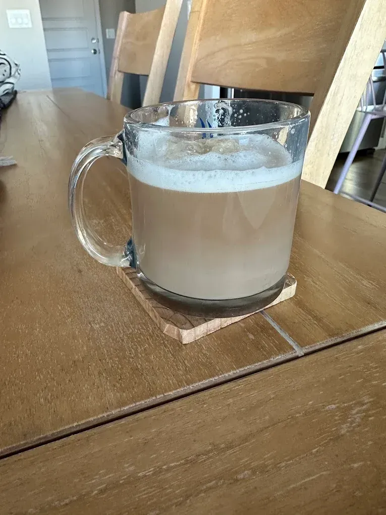 Glass mug of milky coffee on a wooden table in a bright room
