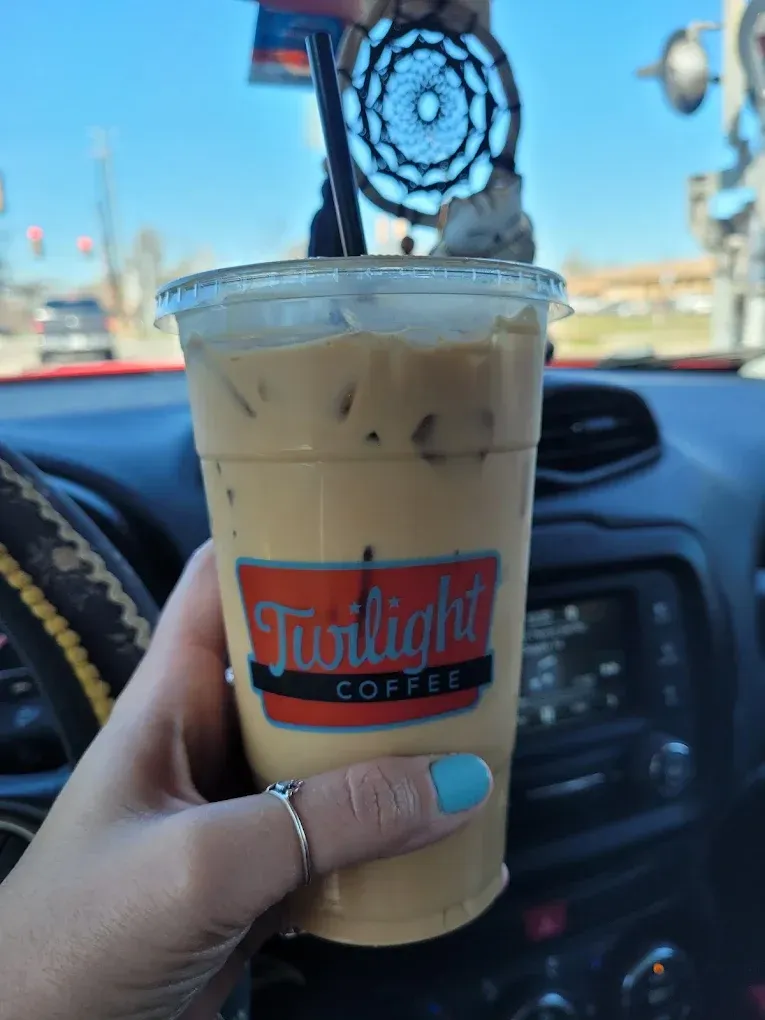 Hand holding iced coffee with a dreamcatcher on the straw, inside a car.