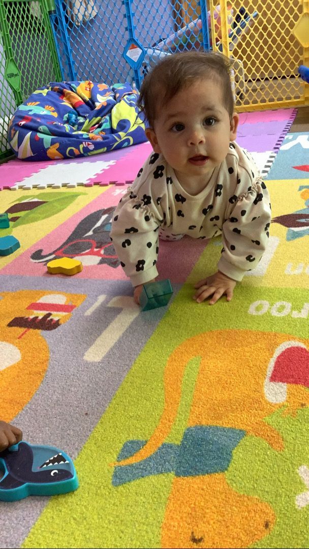 A baby is crawling on a colorful rug on the floor.