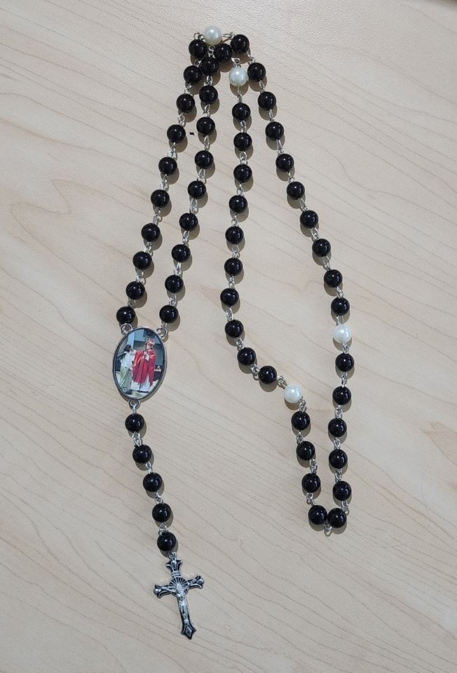 Rosary beads with black and white beads, a crucifix, and a devotional image, laid on wood.