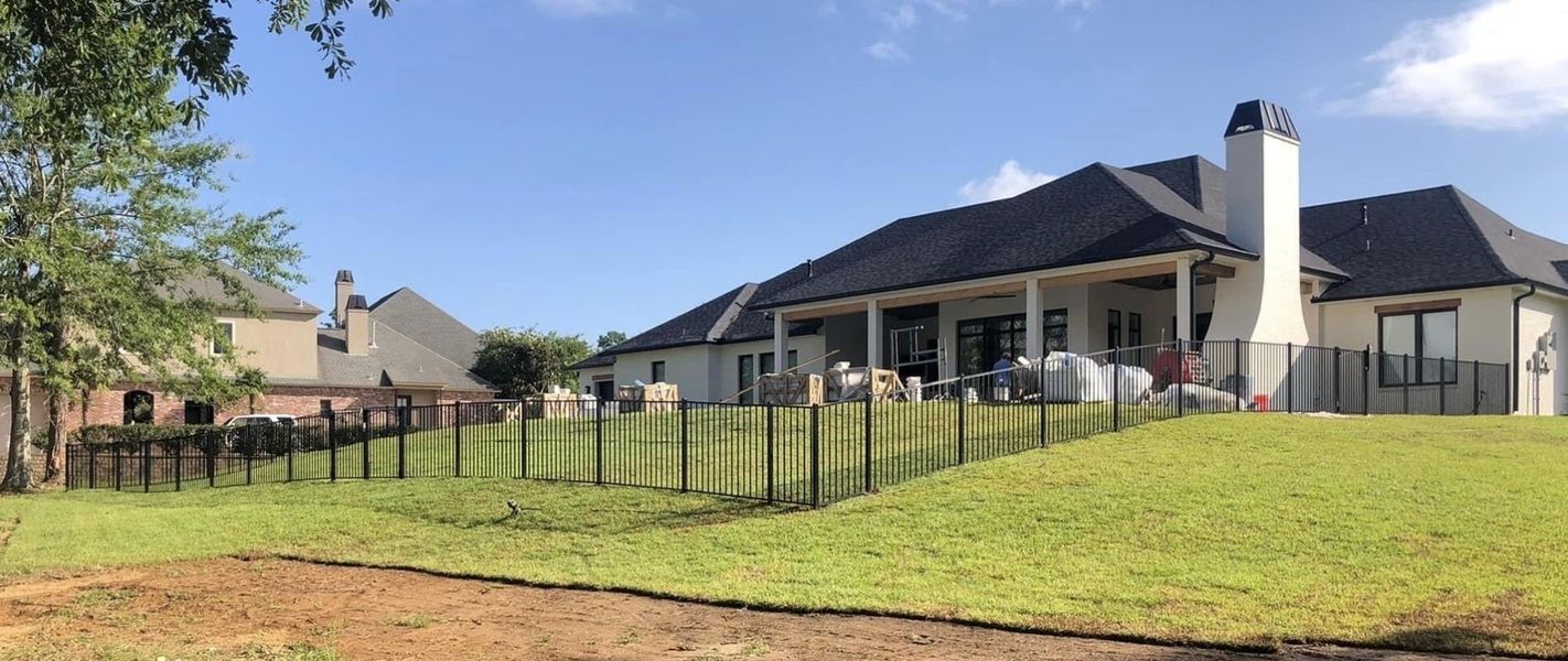 A large house with a fence around it is sitting on top of a lush green hill.