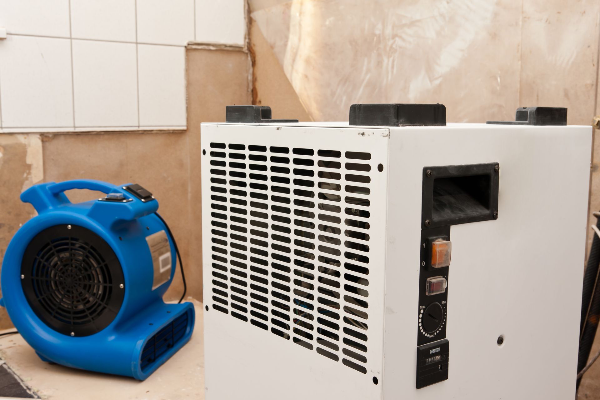 Blue blower fan beside a white industrial dehumidifier in a tiled room