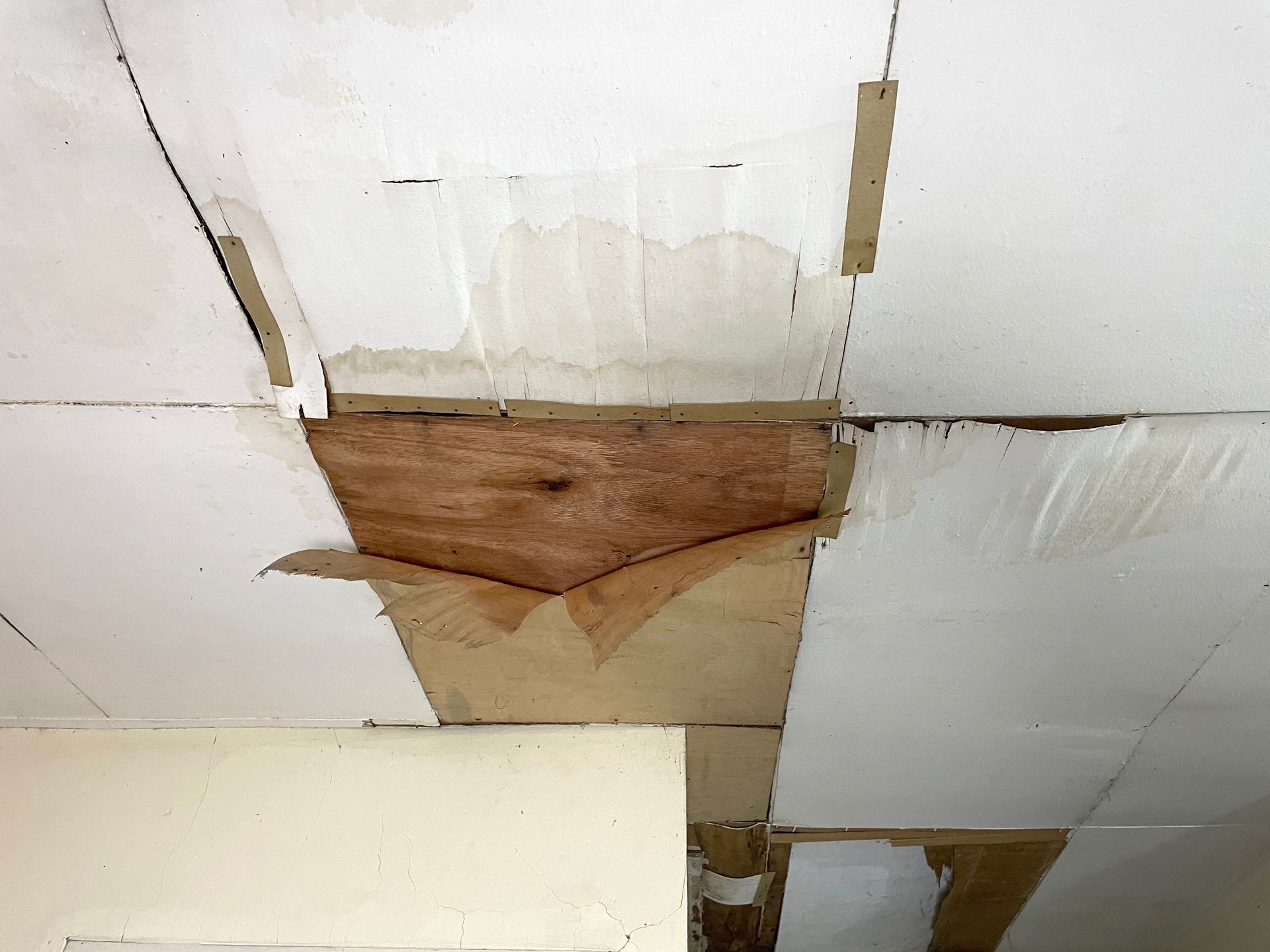 Damaged ceiling with peeling white panels and a large brown water stain and hole