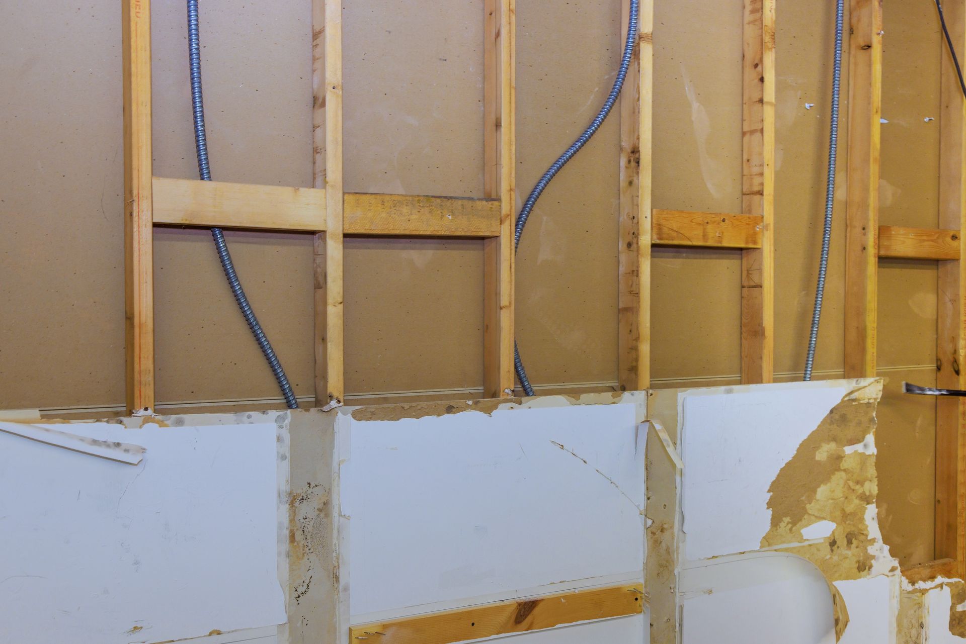 Exposed wall studs with wiring above damaged white drywall panels and peeling paint