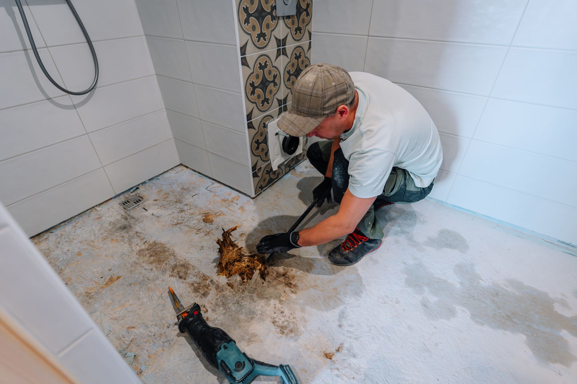 Worker removing moldy floor material in a tiled shower stall with a power tool