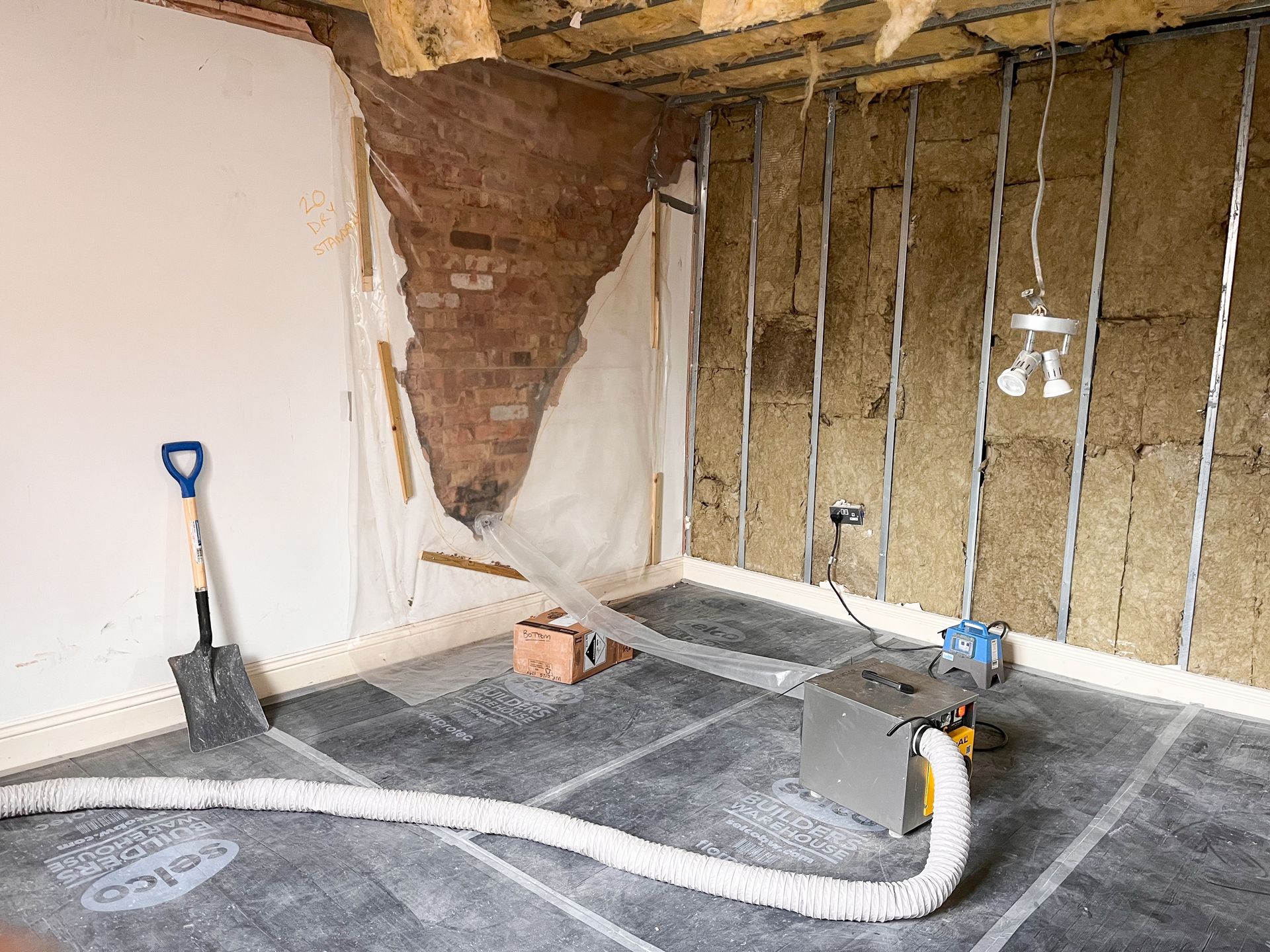 Partially renovated room with exposed brick, insulation, tools, and plastic sheeting on the floor