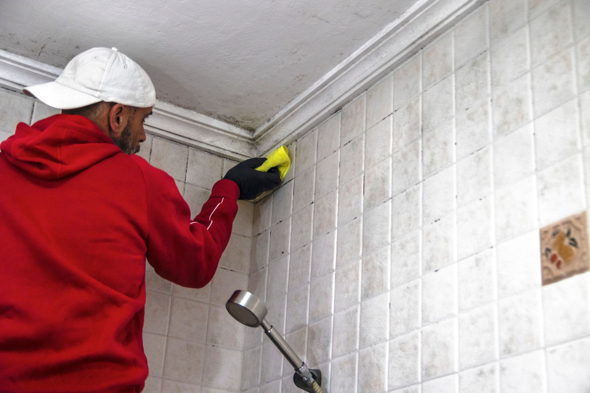 Person in a red hoodie cleaning white tiled wall with a sponge.