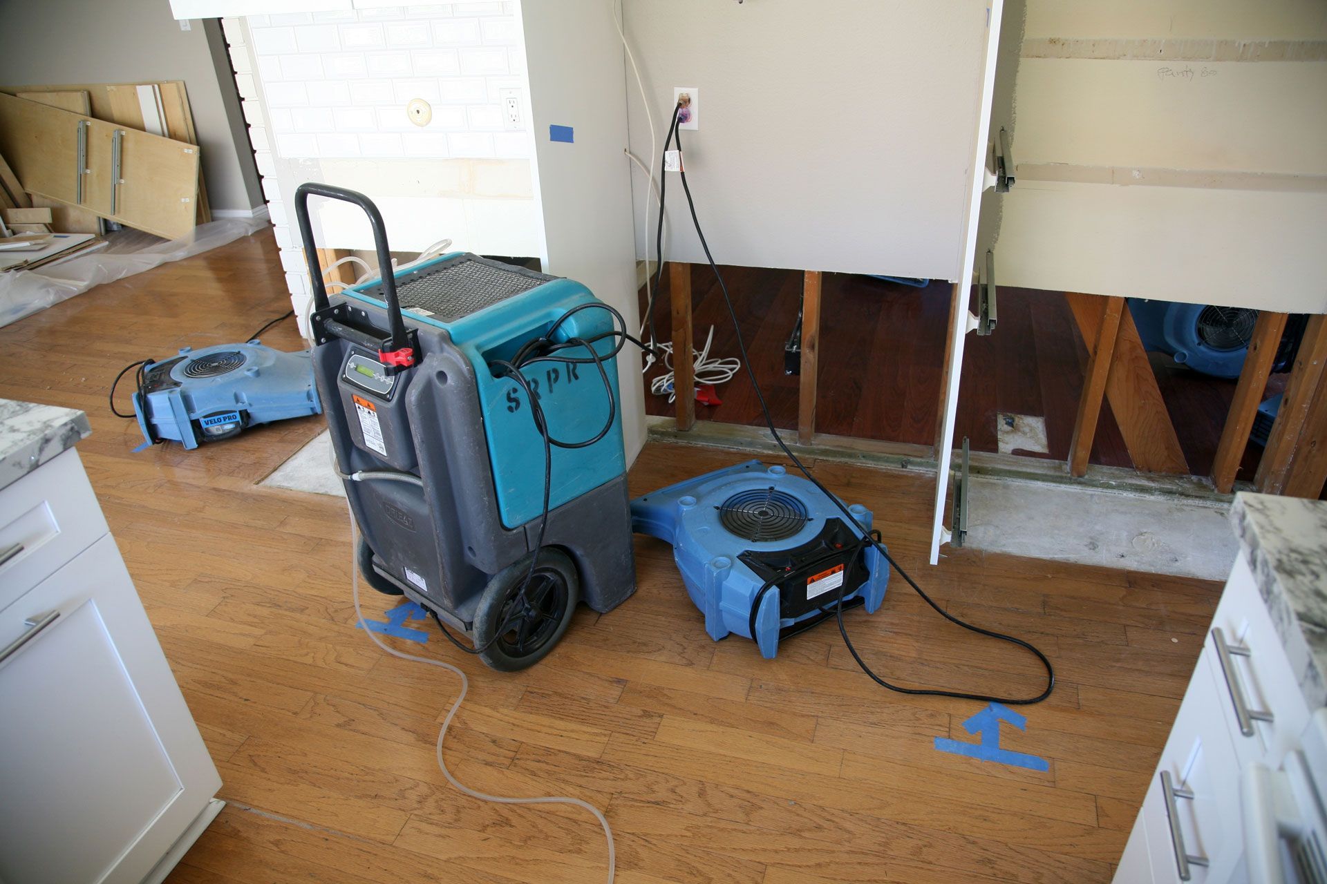 Blue cleaning machine and vacuum in a room with hardwood floor and cabinets, near a wall under repair