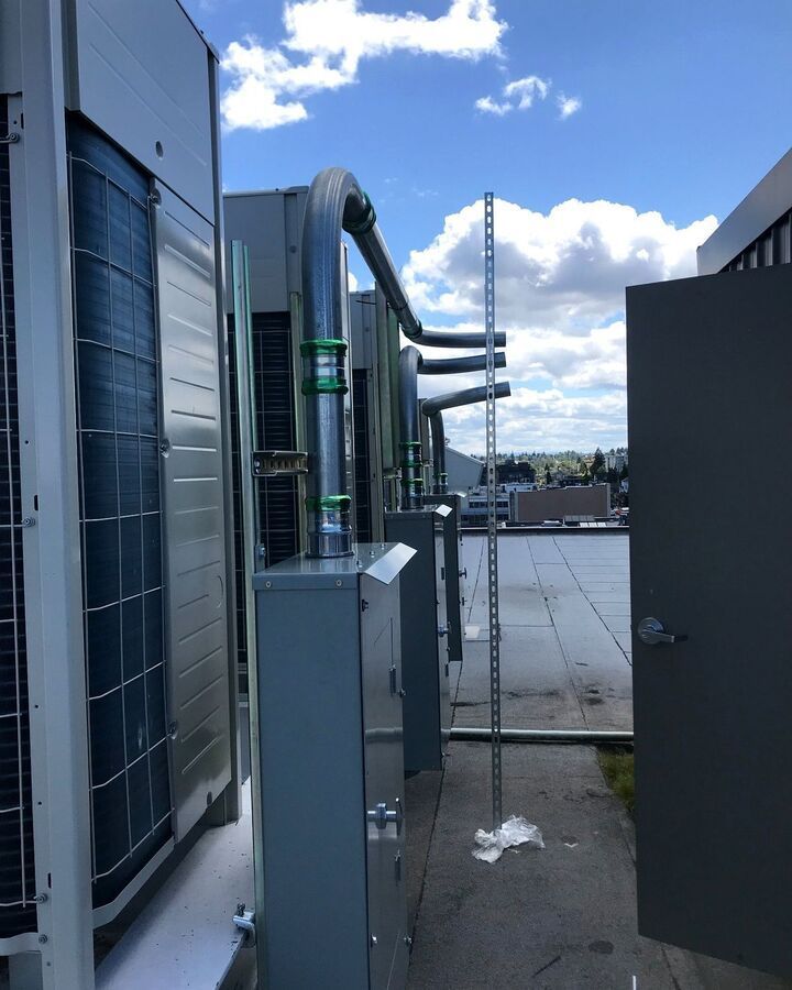Rooftop HVAC units with metal ducts and an open service panel under a cloudy blue sky.