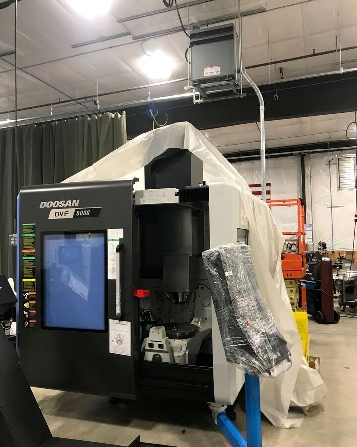 Black Doosan CNC machine in an industrial workshop, partly covered with white plastic sheeting.