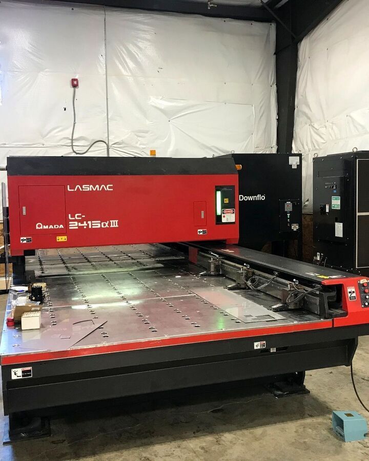Red CNC laser cutting machine in an industrial workshop with metal sheet on the bed.