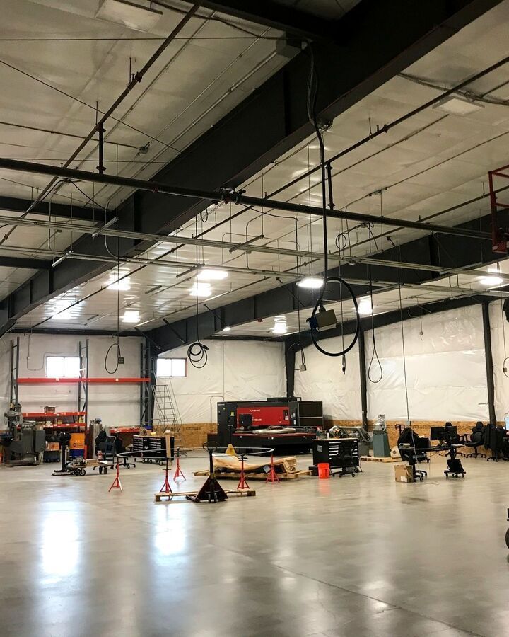 Large industrial warehouse interior with concrete floor, overhead lights, and equipment set up for maintenance or training