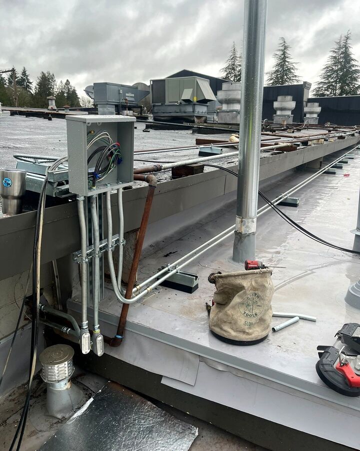 Snow-covered rooftop with HVAC equipment, metal piping, and a vent pipe in the foreground.