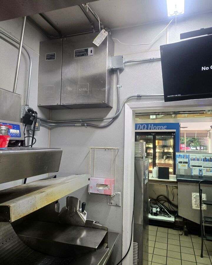 Commercial kitchen with stainless steel equipment, wall-mounted freezer, and an open doorway to a lit back room.