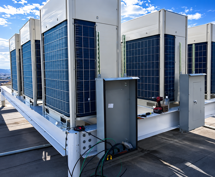 Rooftop HVAC units and ductwork on a commercial building roof under a blue sky.