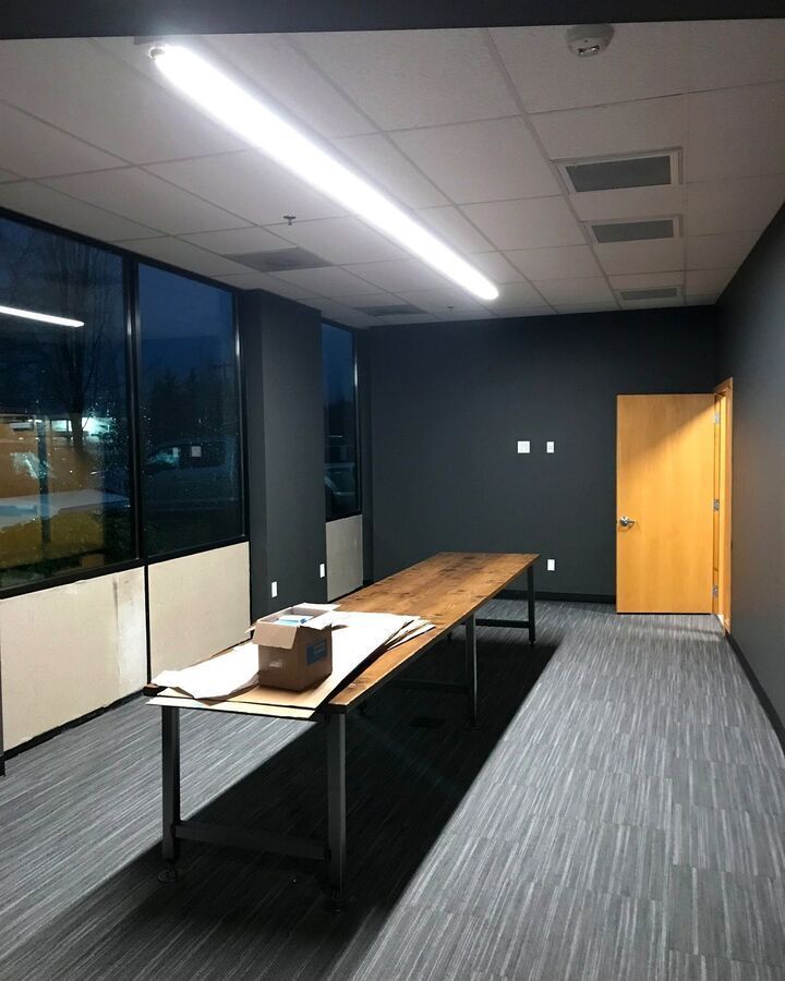 Empty office room with long table, chairs, dark walls, windows, and a wooden door