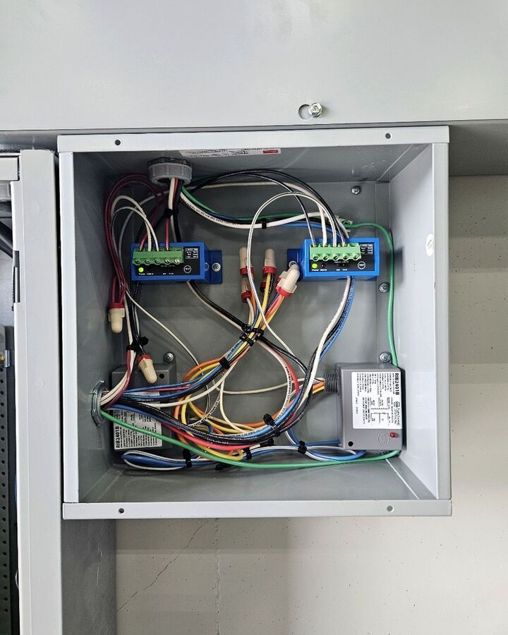 Open electrical control box with tangled multicolor wires, terminal blocks, and a relay module mounted inside.