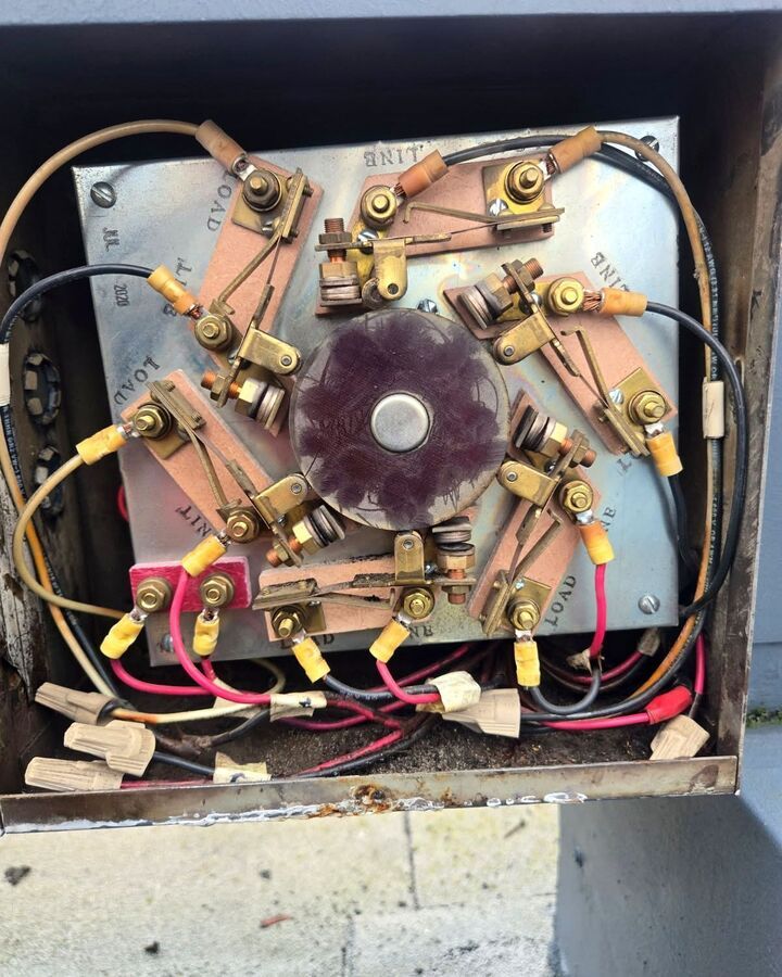 Close-up of a vintage electrical component with wires, brass terminals, and a purple central knob inside a box.