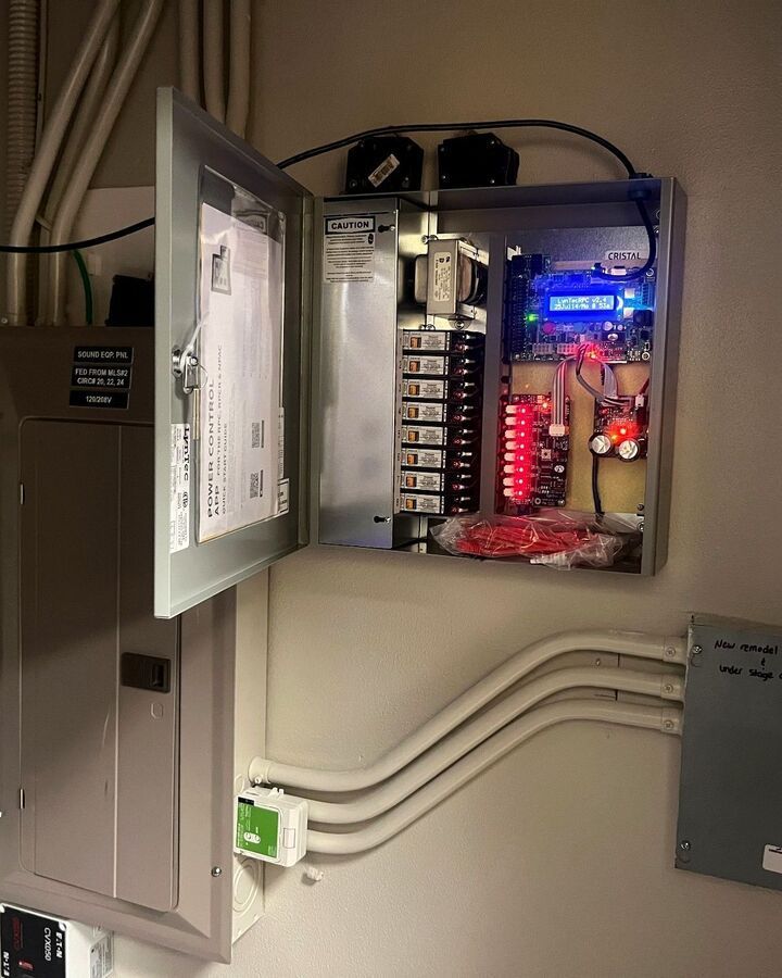 Open electrical control panel with lit circuit board and wiring inside a wall cabinet