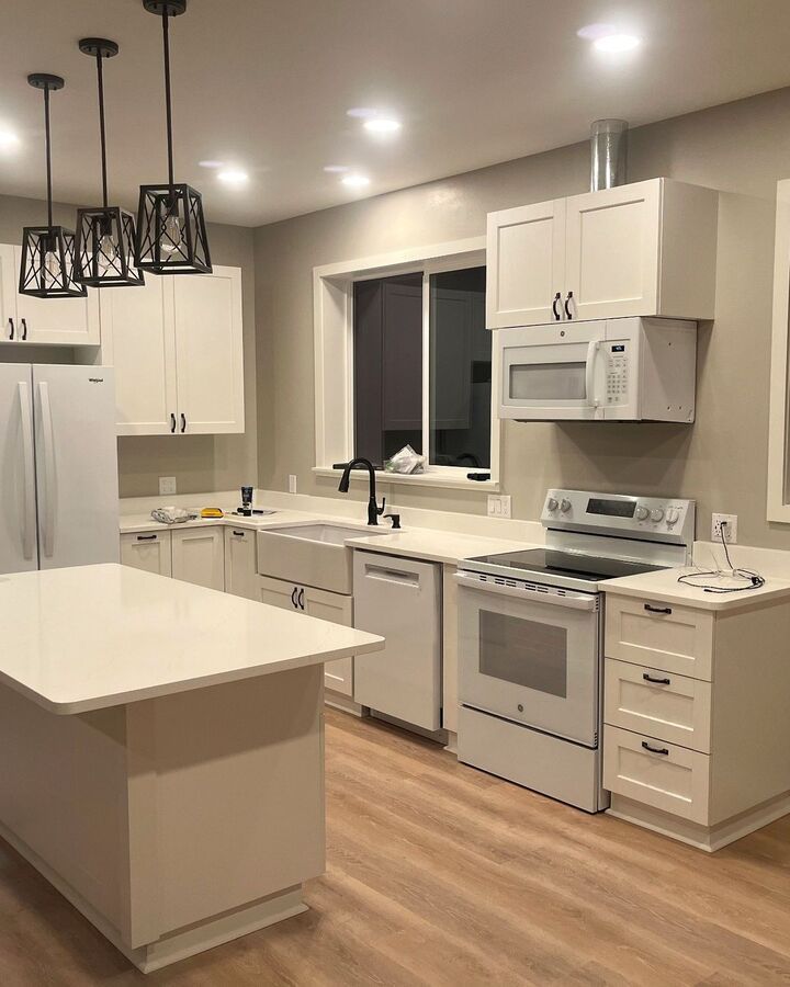 Modern white kitchen with island, stainless appliances, pendant lights, and hardwood floors