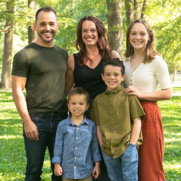 Family of five standing together outdoors on a grassy lawn, smiling at the camera.