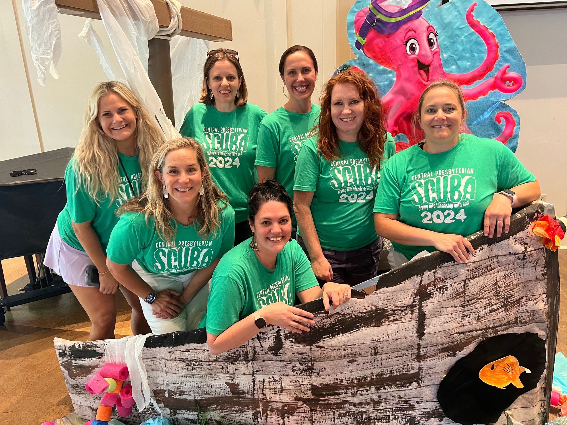 Group in green shirts poses with a large octopus cutout and decorated shark display.