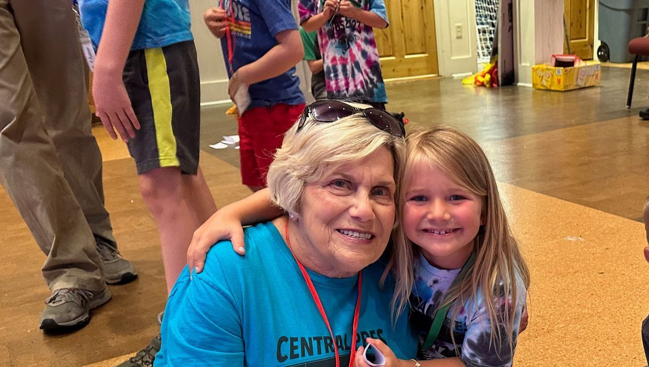 Smiling woman and young girl hugging indoors on a wood floor, both looking at the camera.