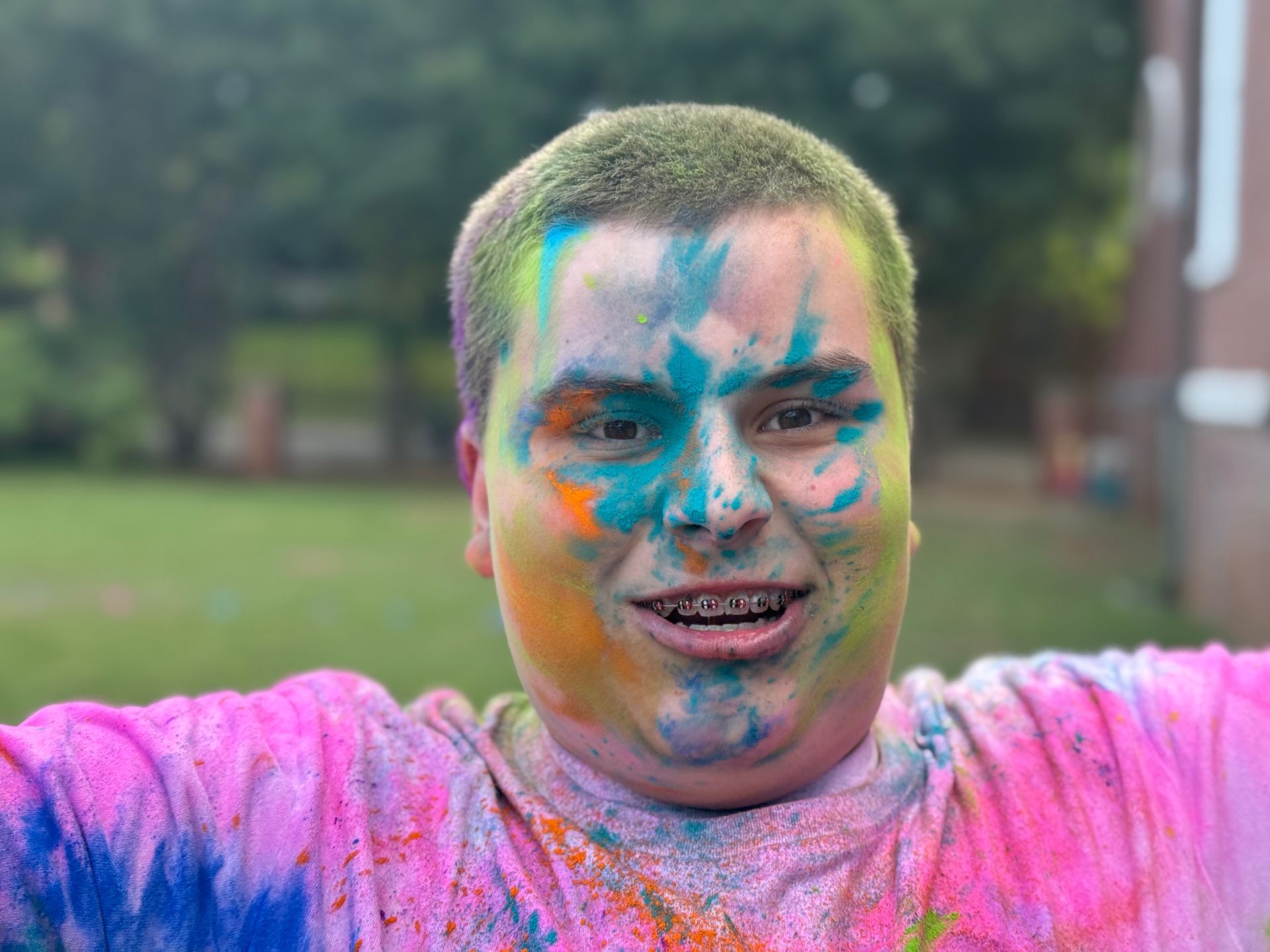 Person outdoors with colorful powder on face and shirt, smiling with arms outstretched
