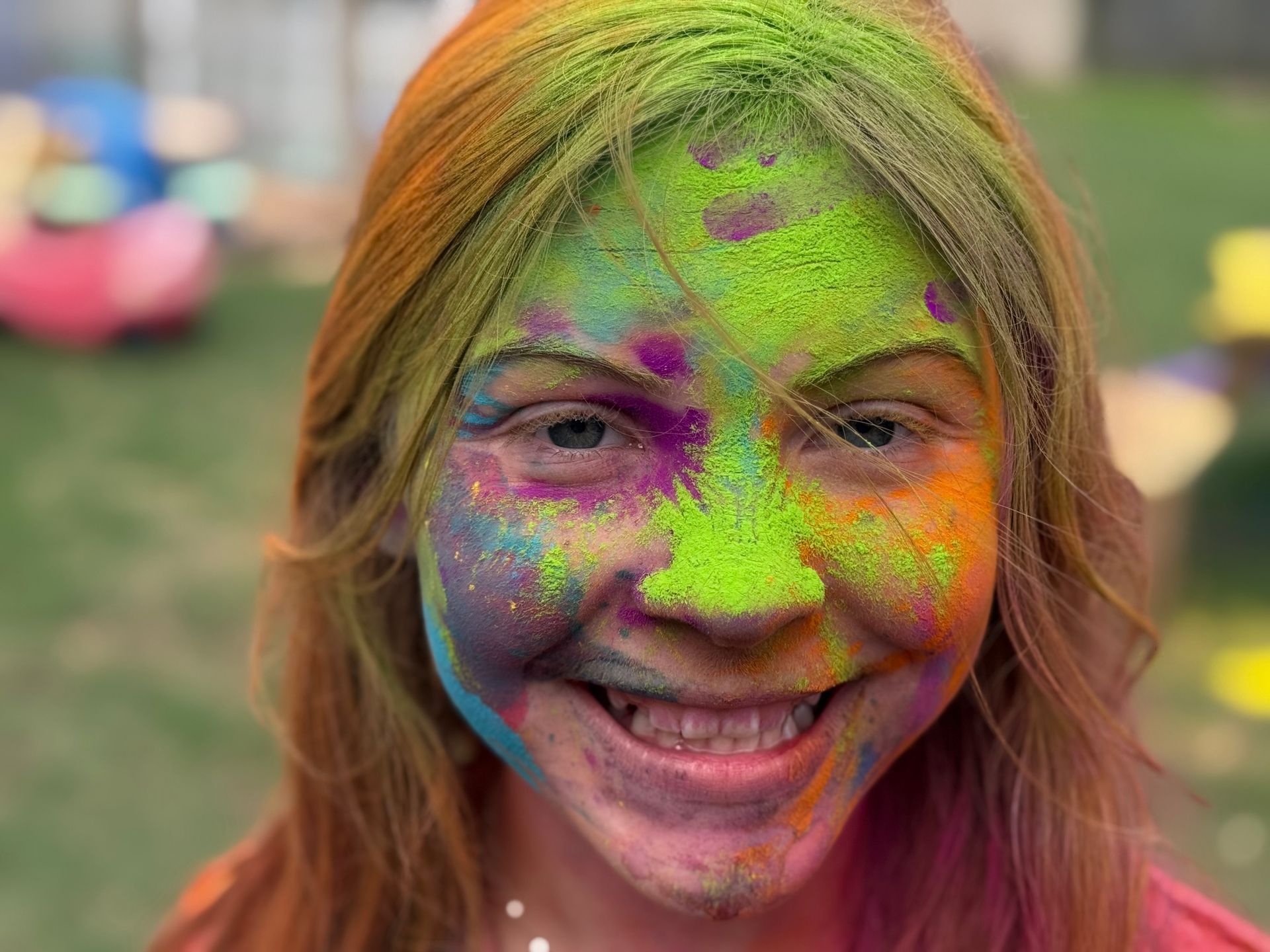 Smiling person with face covered in bright multicolored powder at an outdoor celebration