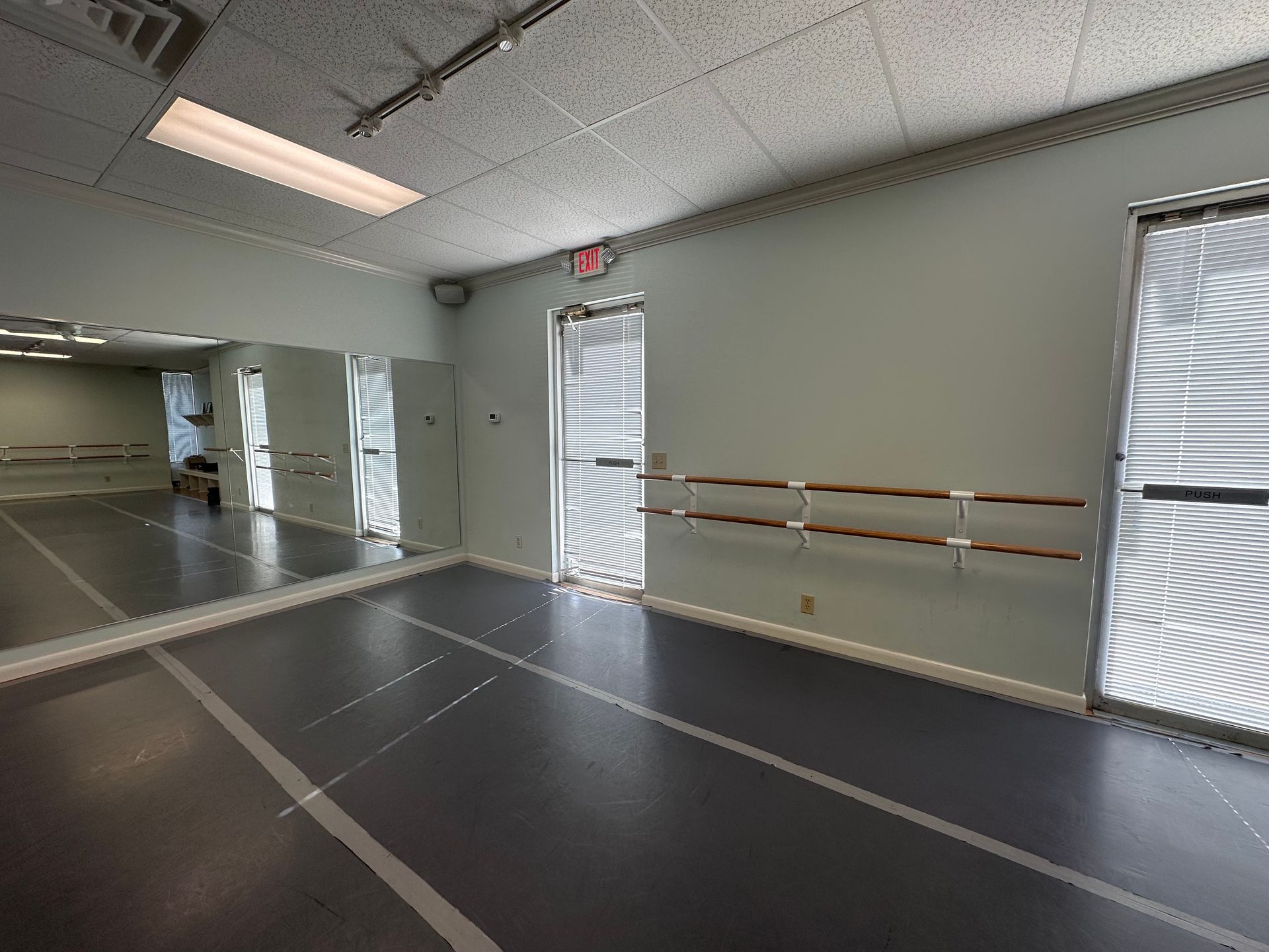 Empty dance studio with mirrors, ballet barres, and a black marley floor under bright ceiling lights